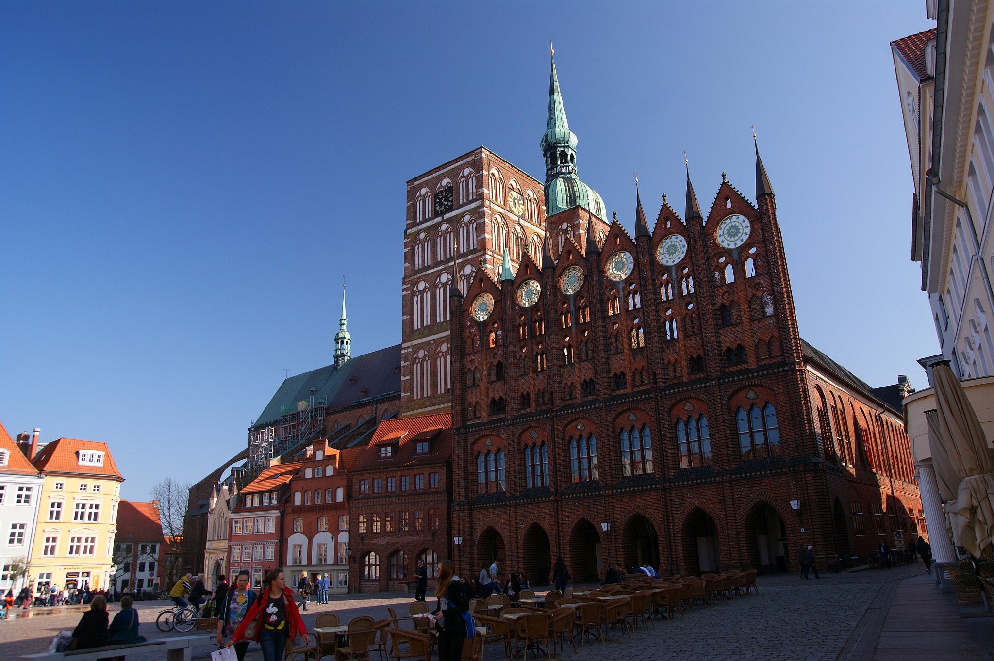 Radnice ve Stralsundu postavená z režného zdiva a z poza ní vykukuje Kostel sv. Mikuláše